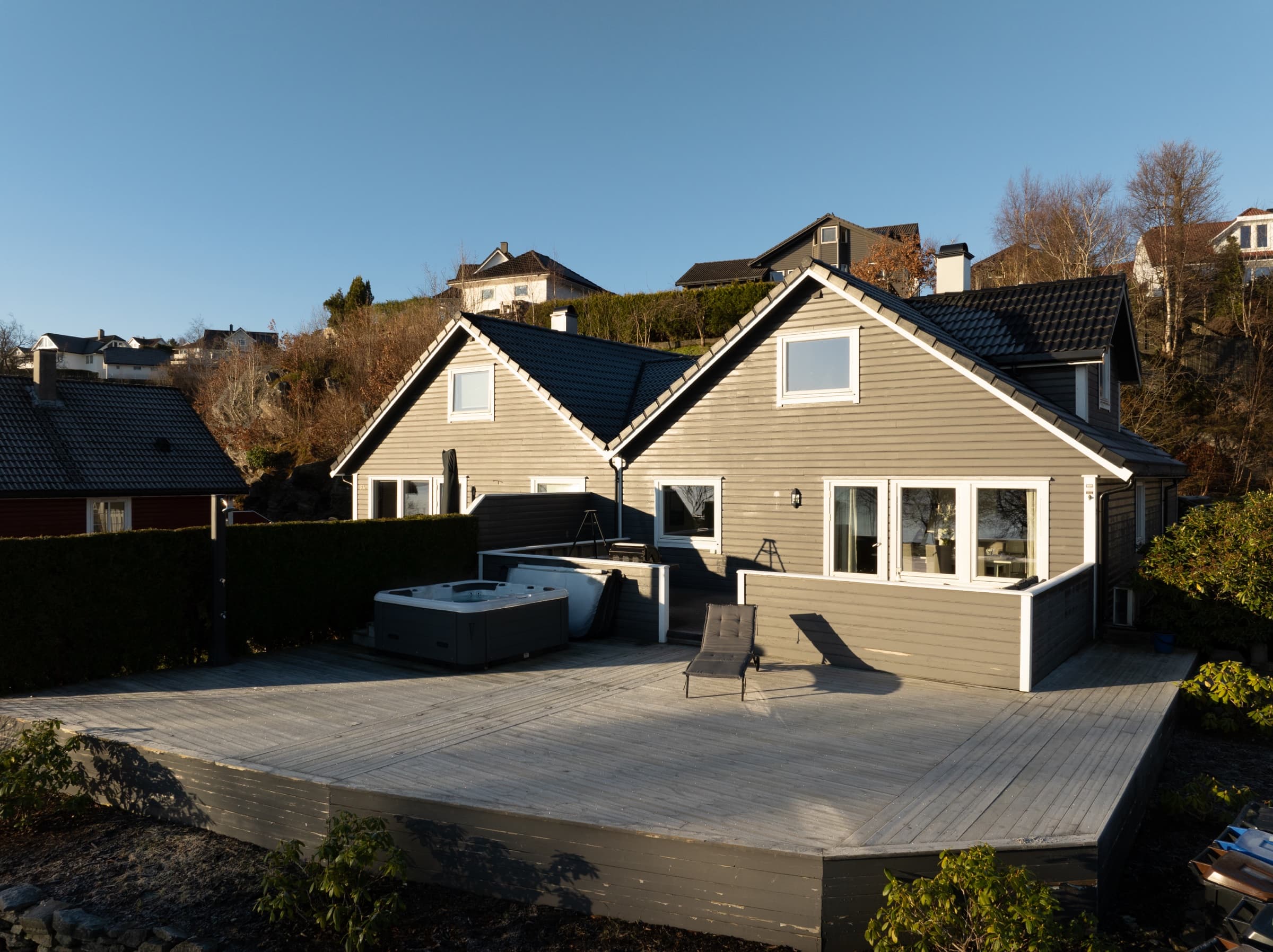 Gray clapboard house with a large wooden deck and hot tub, original unedited photo