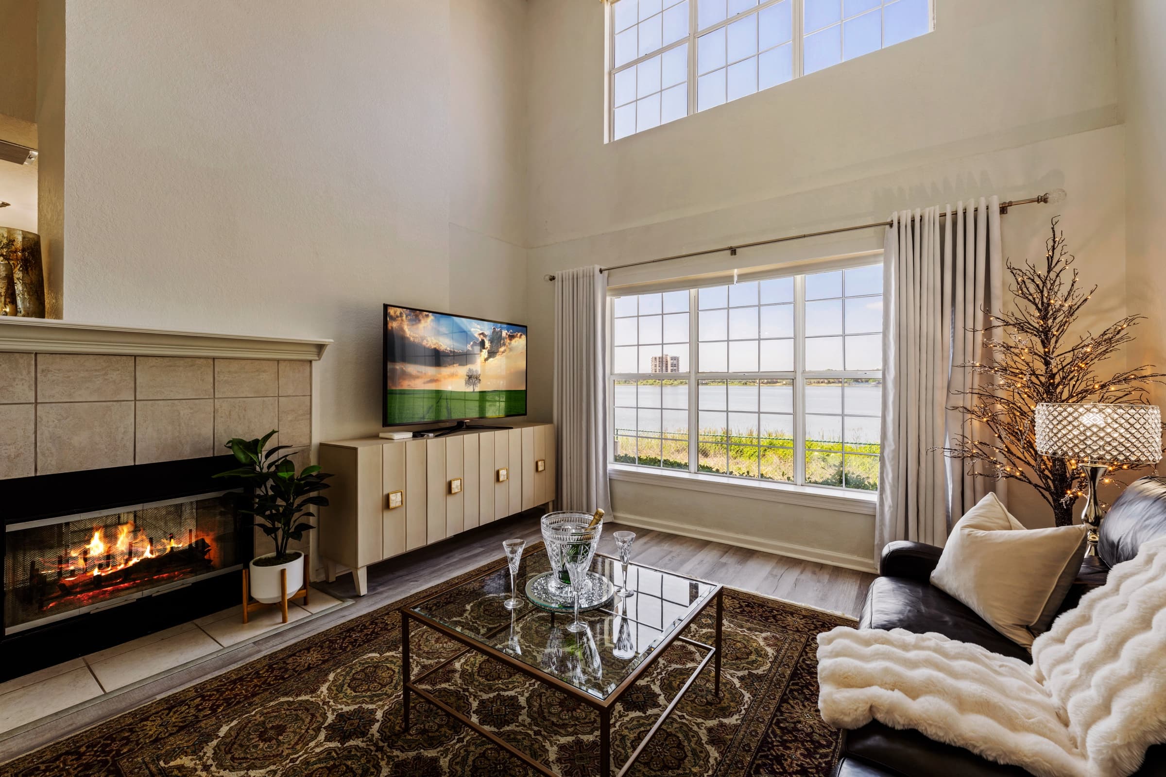The same living room after editing: bright, natural exposure, a clear window view, a lit fireplace and an image on the TV screen