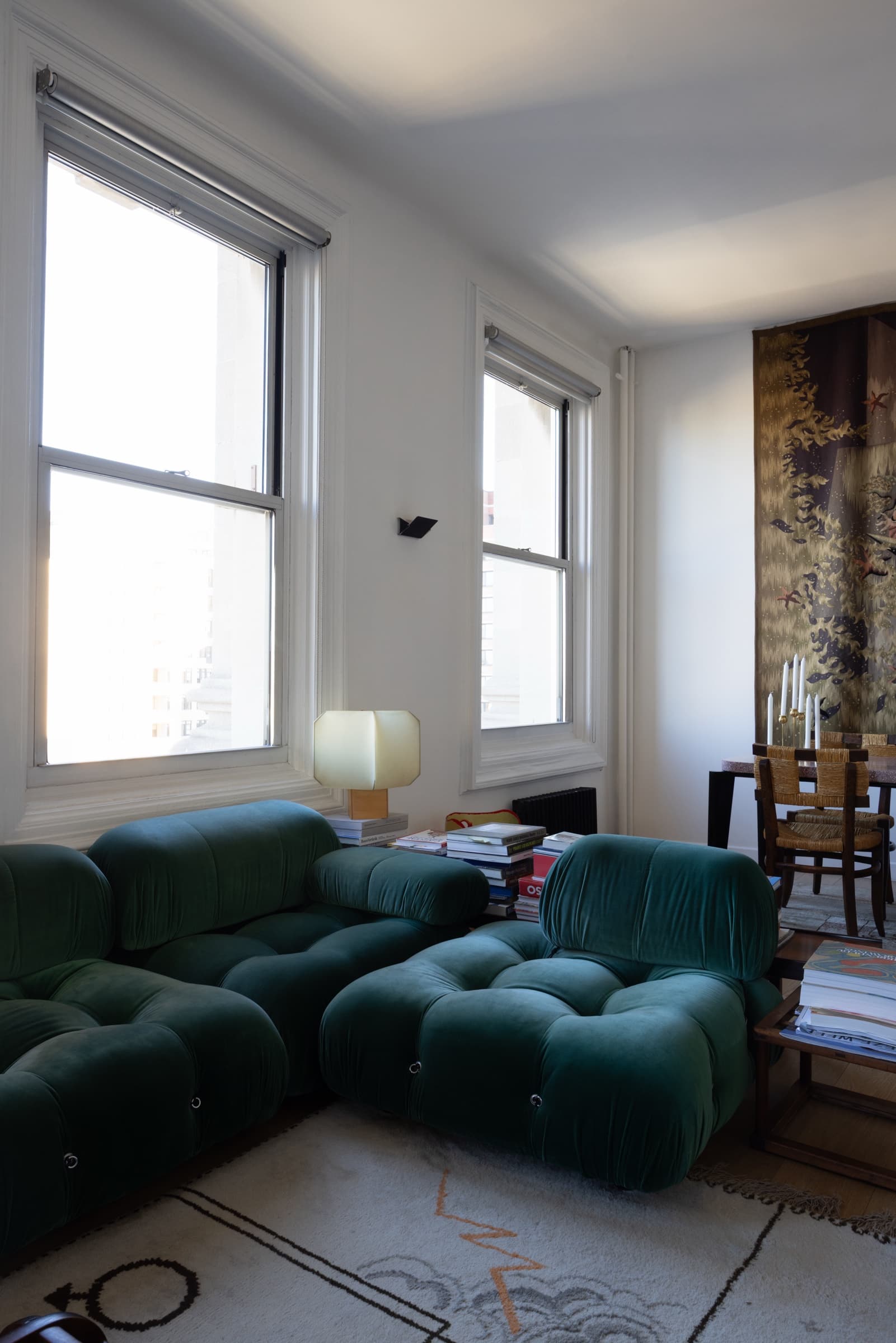 Living room with green velvet modular seating, tall windows and a wall tapestry, original unedited photo