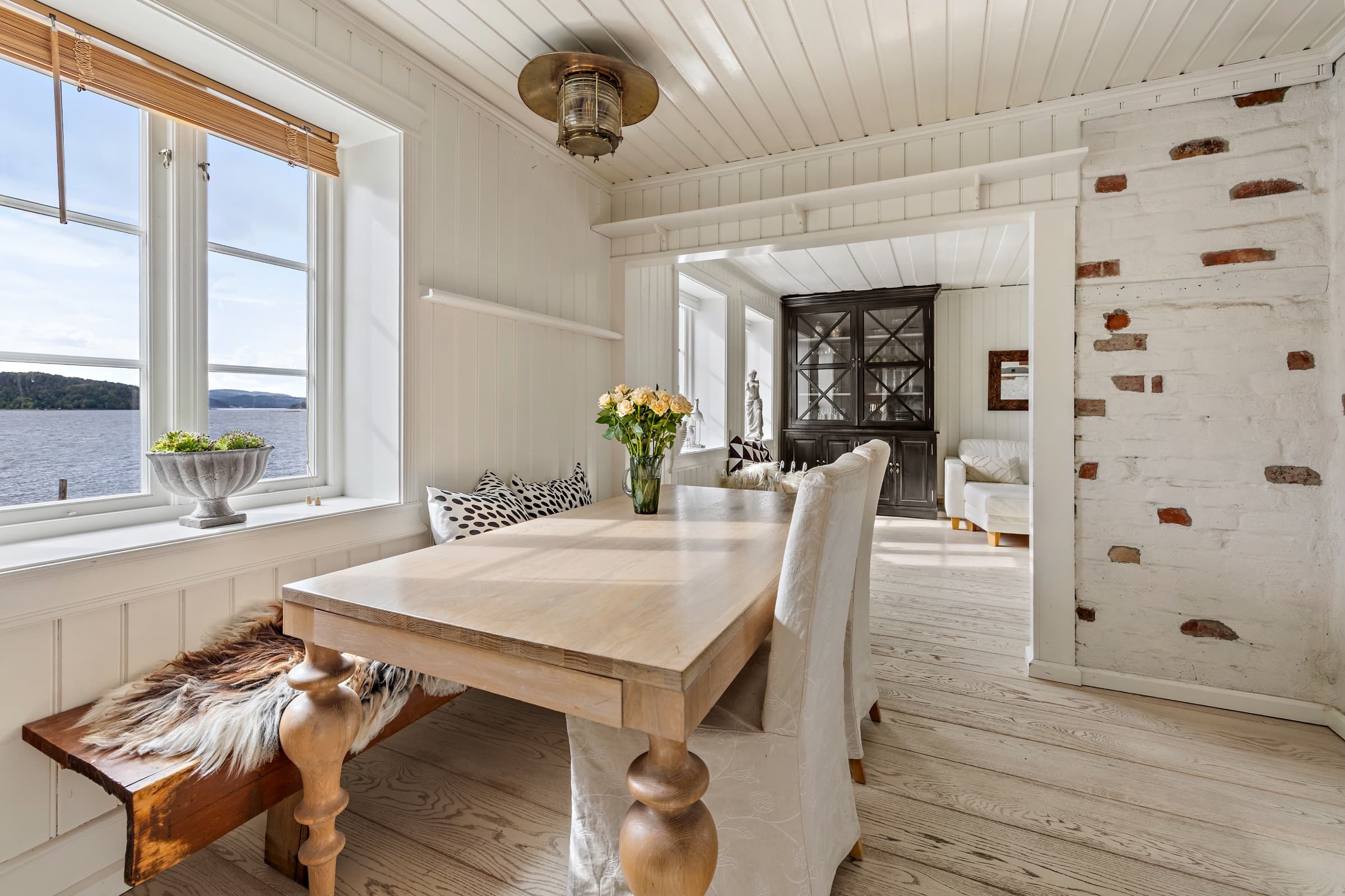 The same dining area after editing: balanced daylight and a clear water view through the window, with wood and brick texture preserved
