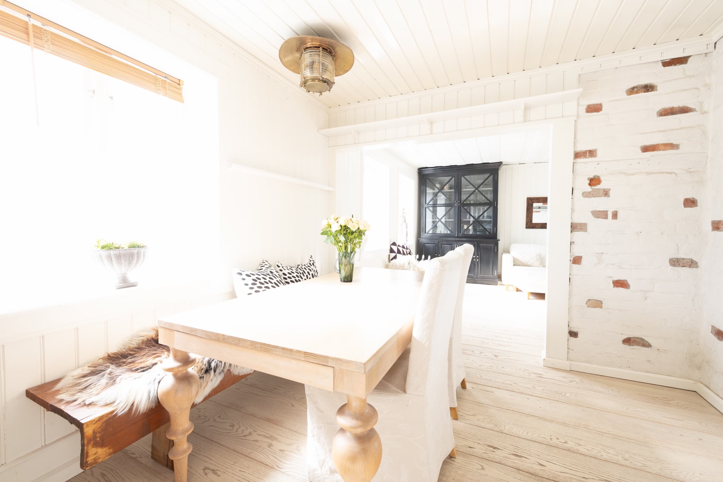Bright dining area with a wooden table, whitewashed brick and an overexposed window, original unedited photo
