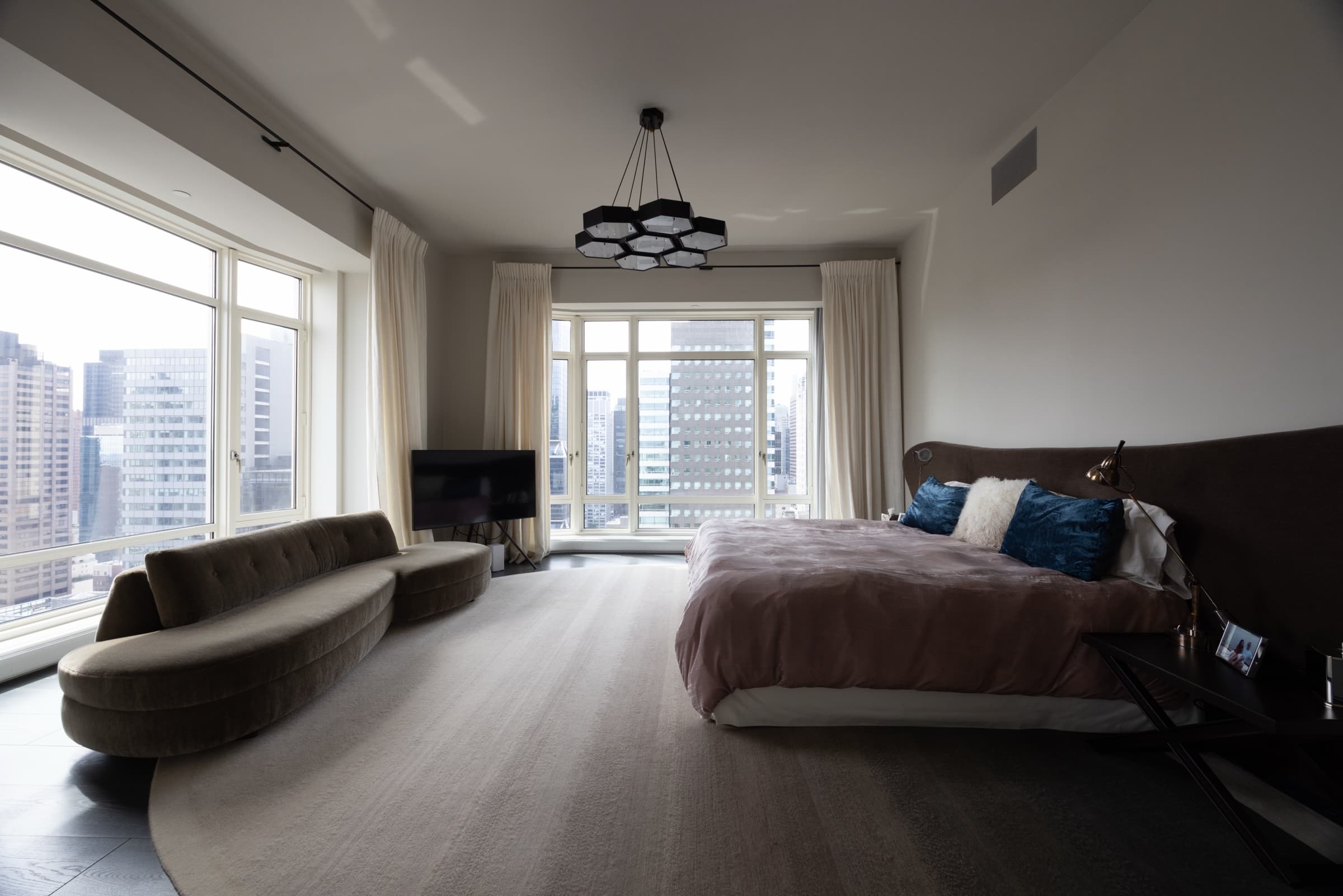 High-rise bedroom with a curved sofa and city-view windows, original unedited photo