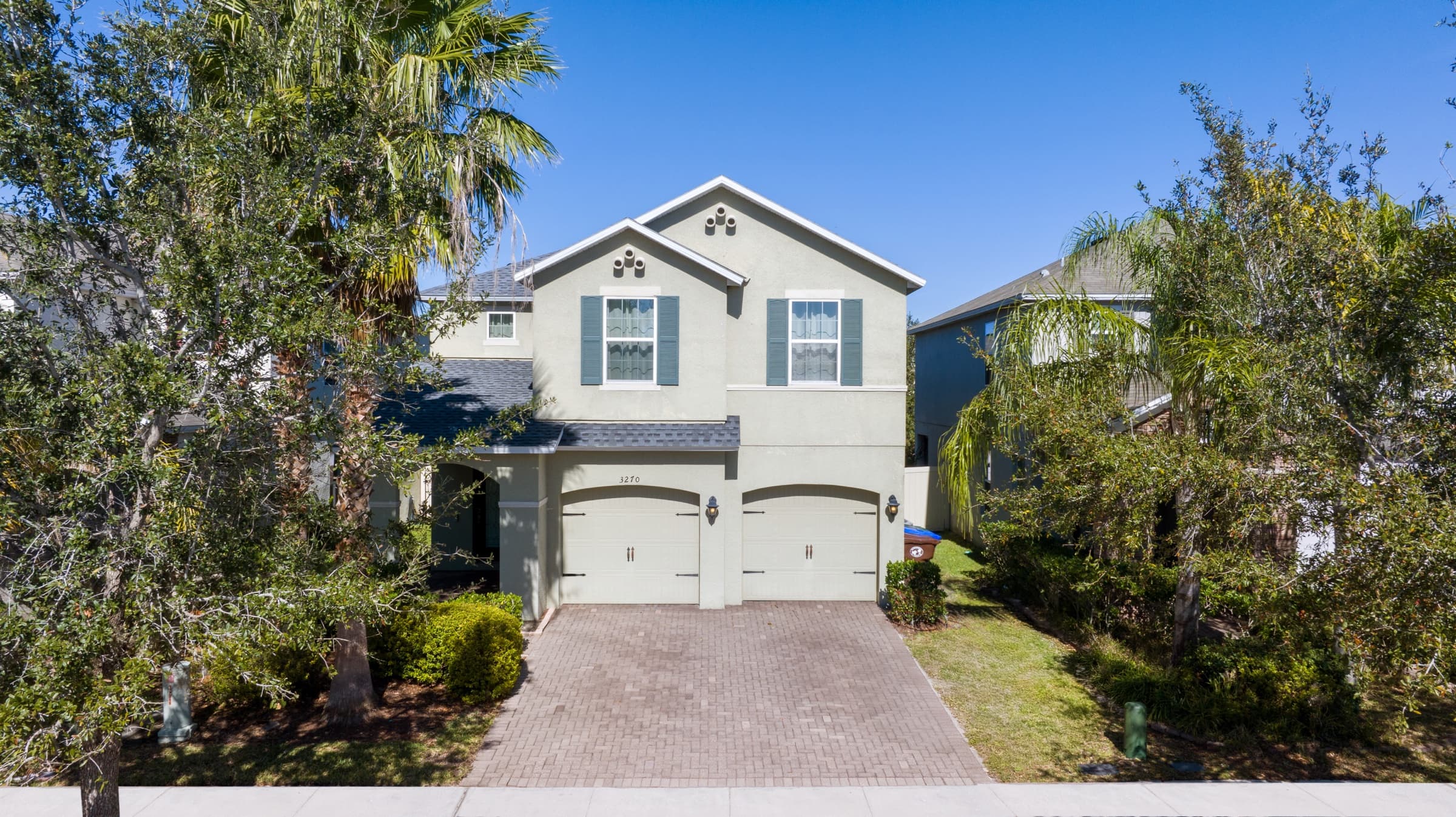 Two-story house with a double garage and palm trees in bright daylight