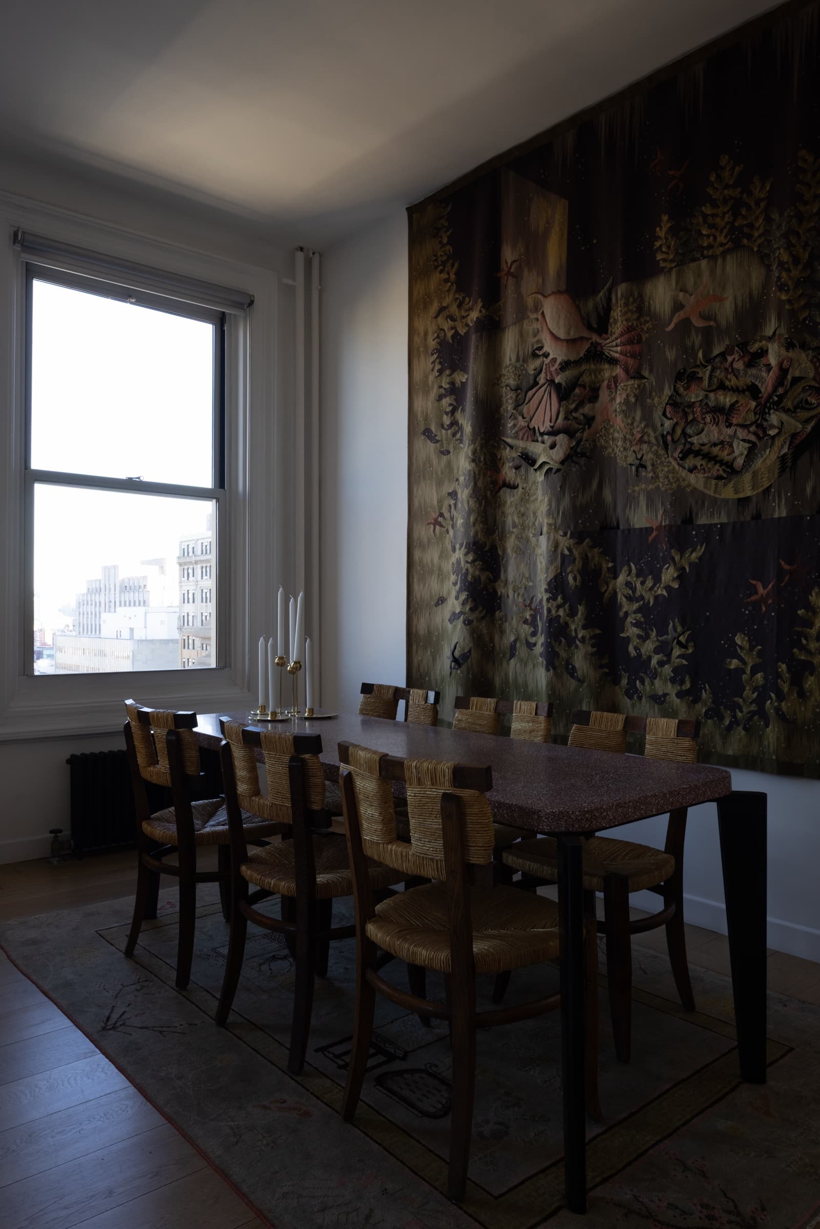 Dining room with rush-seat chairs, a wooden table and a large wall tapestry, original unedited photo