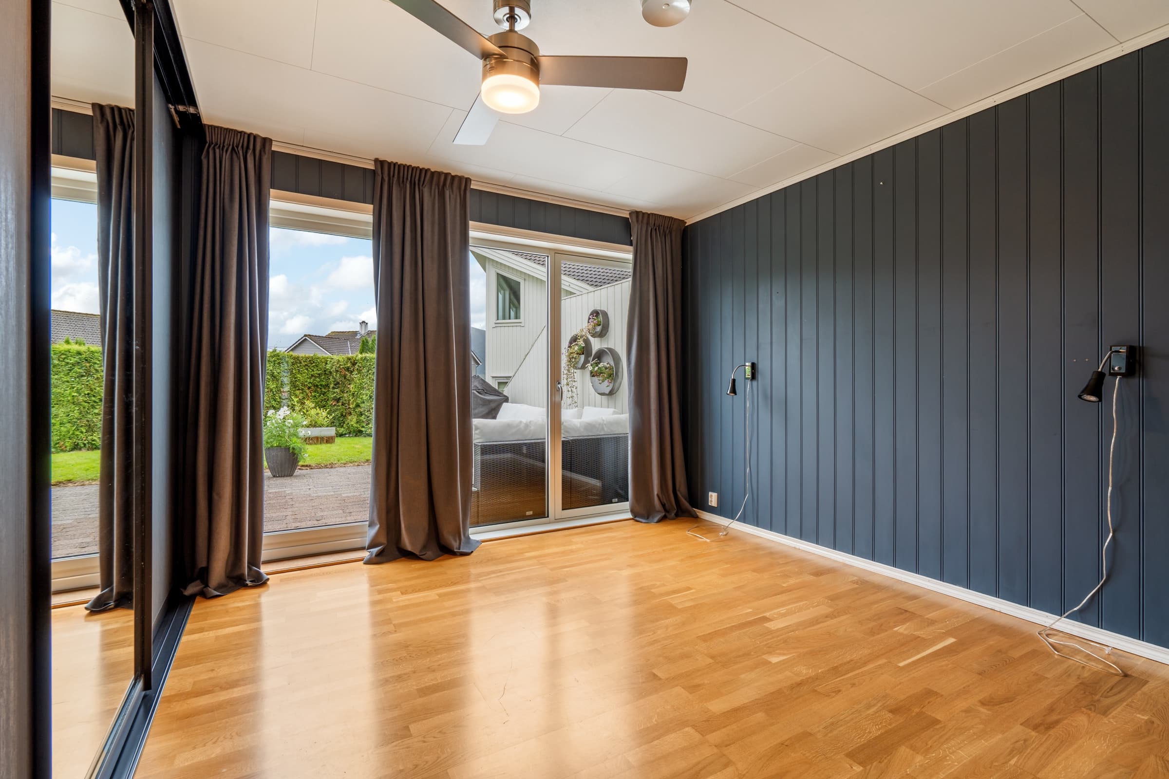 Empty bedroom with a dark paneled wall, wood floor and sliding doors to a garden